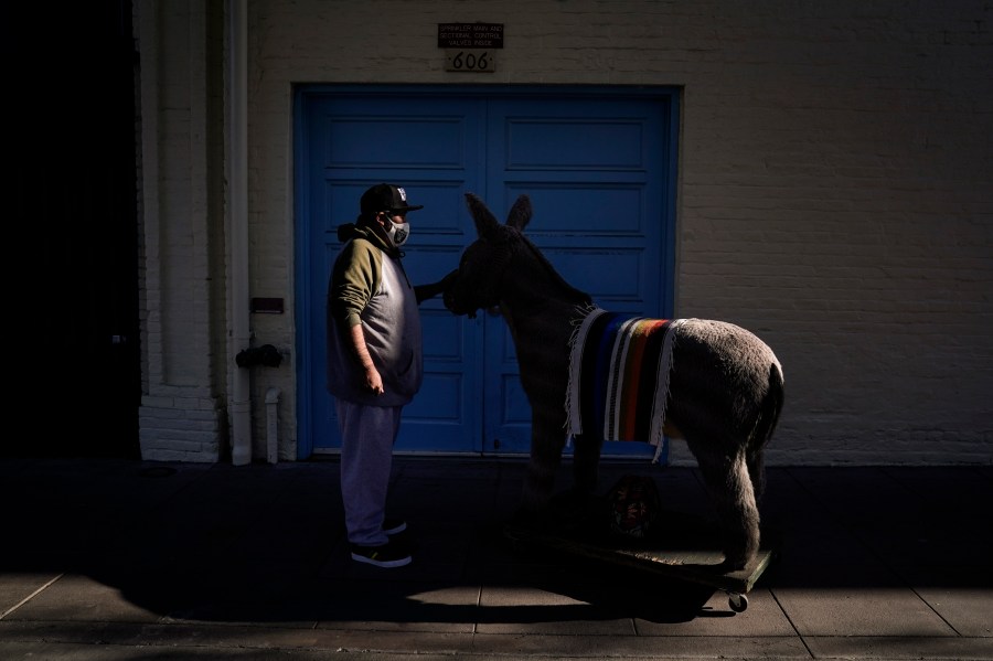 Jesus Hernandez, a merchant who owns a gift shop on Olvera Street that only opens on weekends due to the pandemic, waits for a key to store his uncle's life-size stuffed donkey, a photo prop named George, in downtown Los Angeles, Wednesday, Dec. 16, 2020. Olvera Street, known as the birthplace of Los Angeles, has been particularly hard hit by the coronavirus pandemic, with shops and restaurants closed and others barely hanging on. (Jae C. Hong / Associated Press)