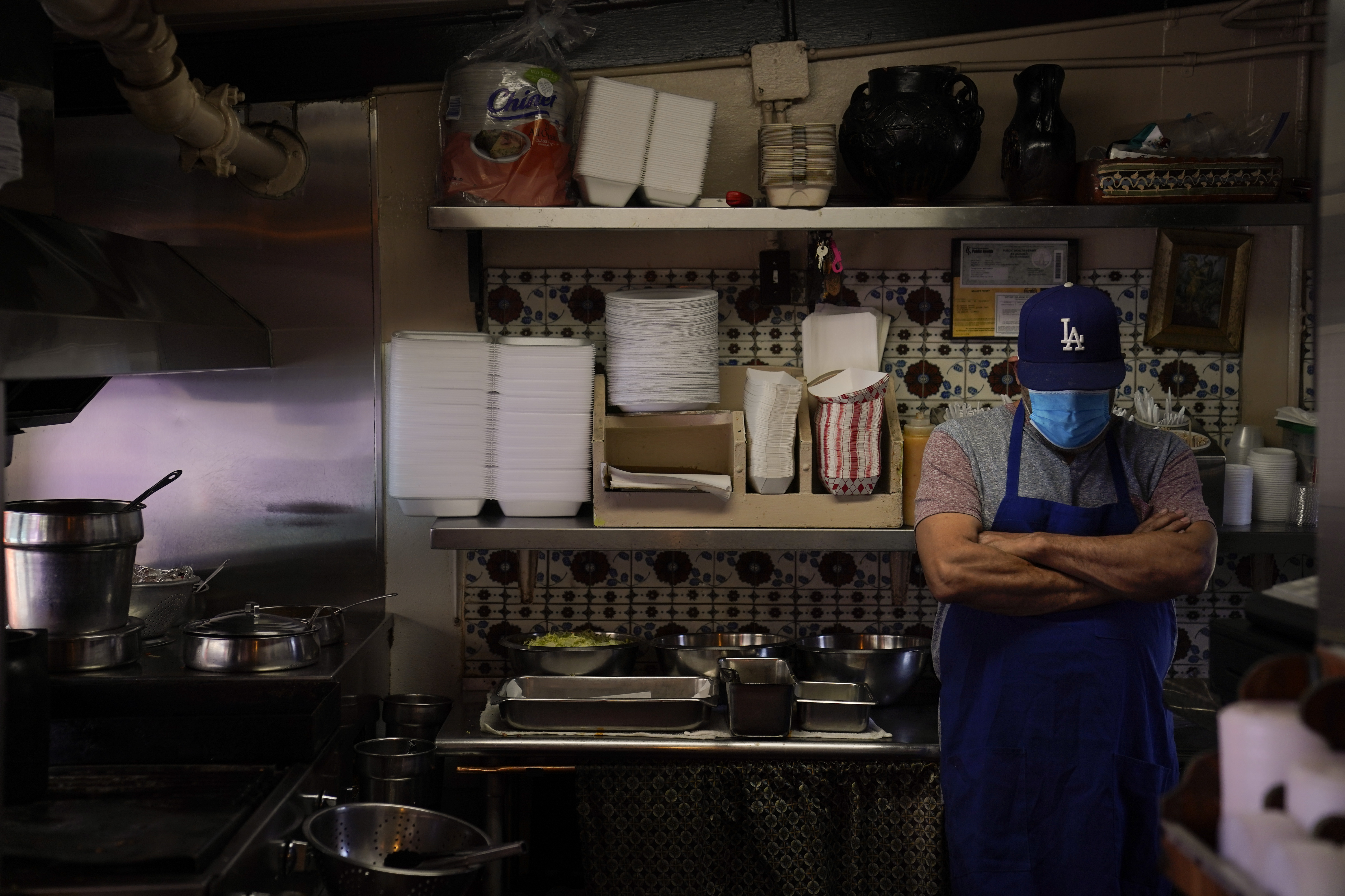 Valo Martinez, a 63-year-old cook working at El Rancho Grande, waits for customers on Olvera Street in downtown Los Angeles, Wednesday, Dec. 16, 2020. The tree-covered brick alley typically teeming with tourists is empty. Many of the shops that sell everything from traditional Mexican folk dresses to paintings of artist Frida Kahlo to sombreros are padlocked and the ones open have few, if any, customers. (Jae C. Hong / Associated Press)