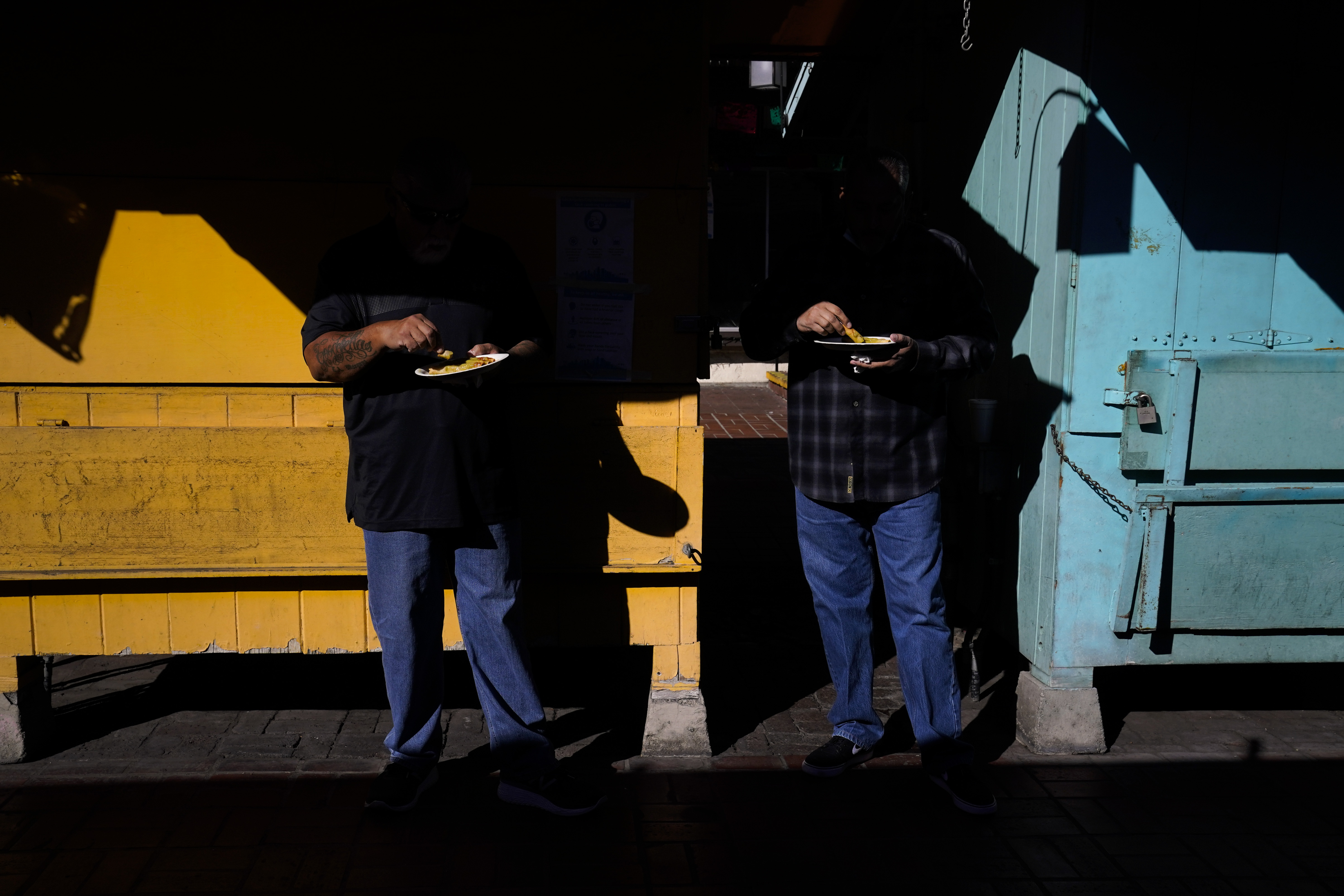 Two customers eat their lunch in front of shuttered market stalls on Olvera Street in downtown Los Angeles, Wednesday, Dec. 16, 2020. Olvera Street, known as the birthplace of Los Angeles, has been particularly hard hit by the coronavirus pandemic, with shops and restaurants closed and others barely hanging on. Only a handful of businesses remain open on weekdays as tourism has cratered and downtown offices are closed and festive events held throughout the year have been canceled. (Jae C. Hong / Associated Press)