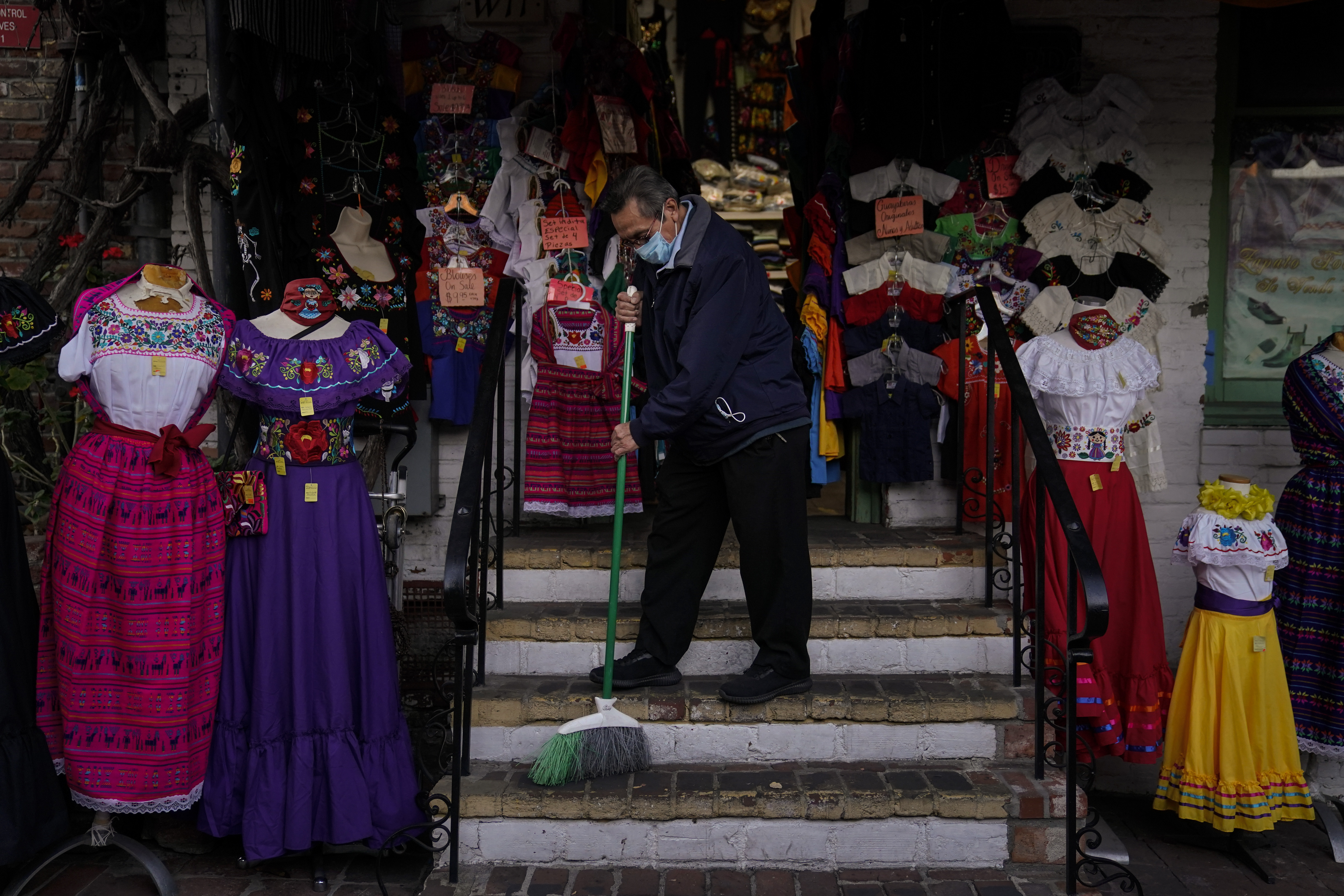 Victor Flores, 66, a third-generation owner of a gift shop, sweeps the steps of his store on Olvera Street in downtown Los Angeles on Dec. 16, 2020. (Jae C. Hong / Associated Press)