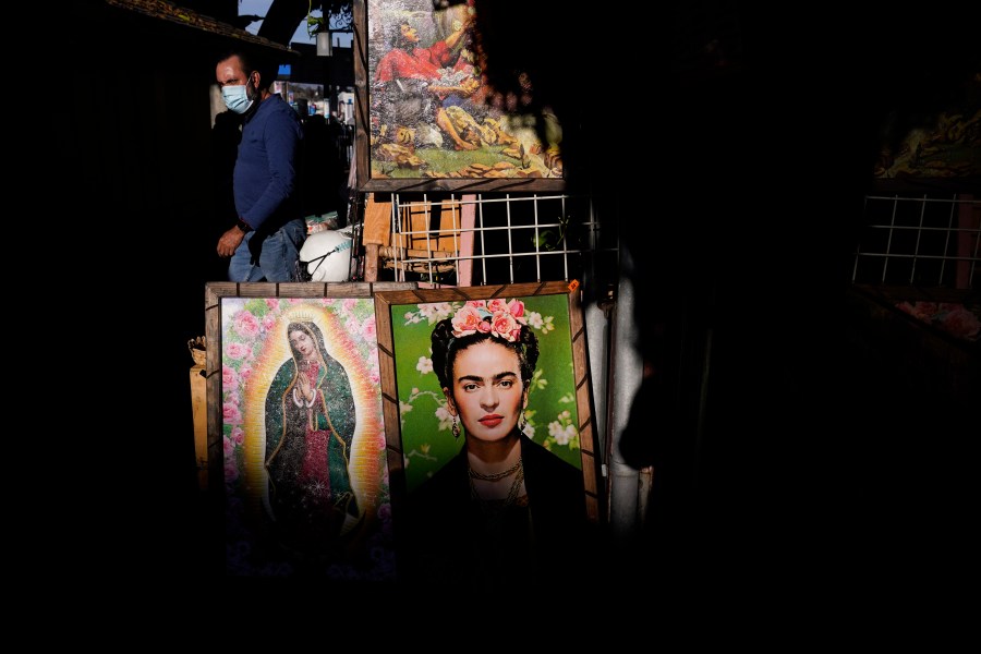 Framed paintings depicting Our Lady of Guadalupe and Mexican artist Frida Kahlo are placed outside a gift shop on Olvera Street in downtown Los Angeles, Wednesday, Dec. 16, 2020. The tree-covered brick alley typically teeming with tourists is empty. Many of the shops that sell everything from traditional Mexican folk dresses to paintings of artist Frida Kahlo to sombreros are padlocked and the ones open have few, if any, customers. (Jae C. Hong / Associated Press)