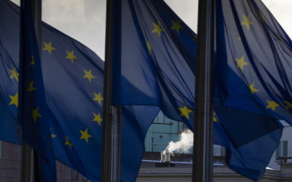 Smoke rises from a chimney behind EU flags fluttering in the wind outside EU headquarters in Brussels, Thursday, Dec. 24, 2020. (AP Photo/Virginia Mayo)