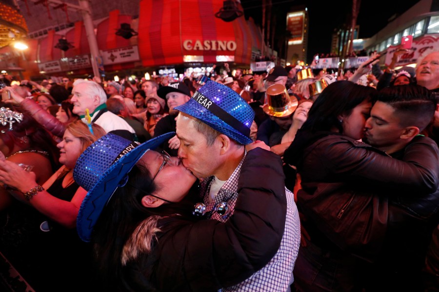 In this Jan. 1, 2018, file photo, newlyweds Alison and Kenny Finchum, lower left, of Tulsa, Okla., kiss just after midnight during a New Year's party at the Fremont Street Experience in downtown Las Vegas. (Steve Marcus/Las Vegas Sun via AP)