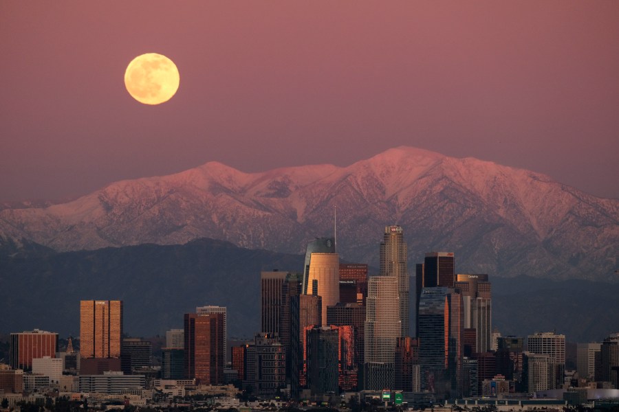 The moon rises over snow-covered mountains, behind the downtown Los Angeles skyline as seen from Kenneth Hahn State Recreation Area Tuesday, Dec. 29, 2020, in Los Angeles. (AP Photo/Ringo H.W. Chiu)