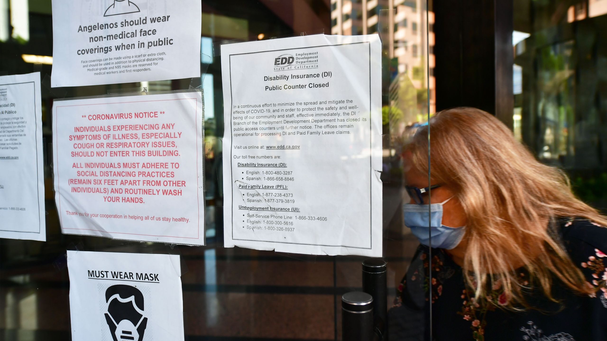 A woman wearing a facemask enters a building where the Employment Development Department has its offices in Los Angeles, California on May 4, 2020, past a posted sign mentioning the closure of the offices's public access counters due to the coronavirus pandemic. (Frederic J. Brown/AFP via Getty Images)