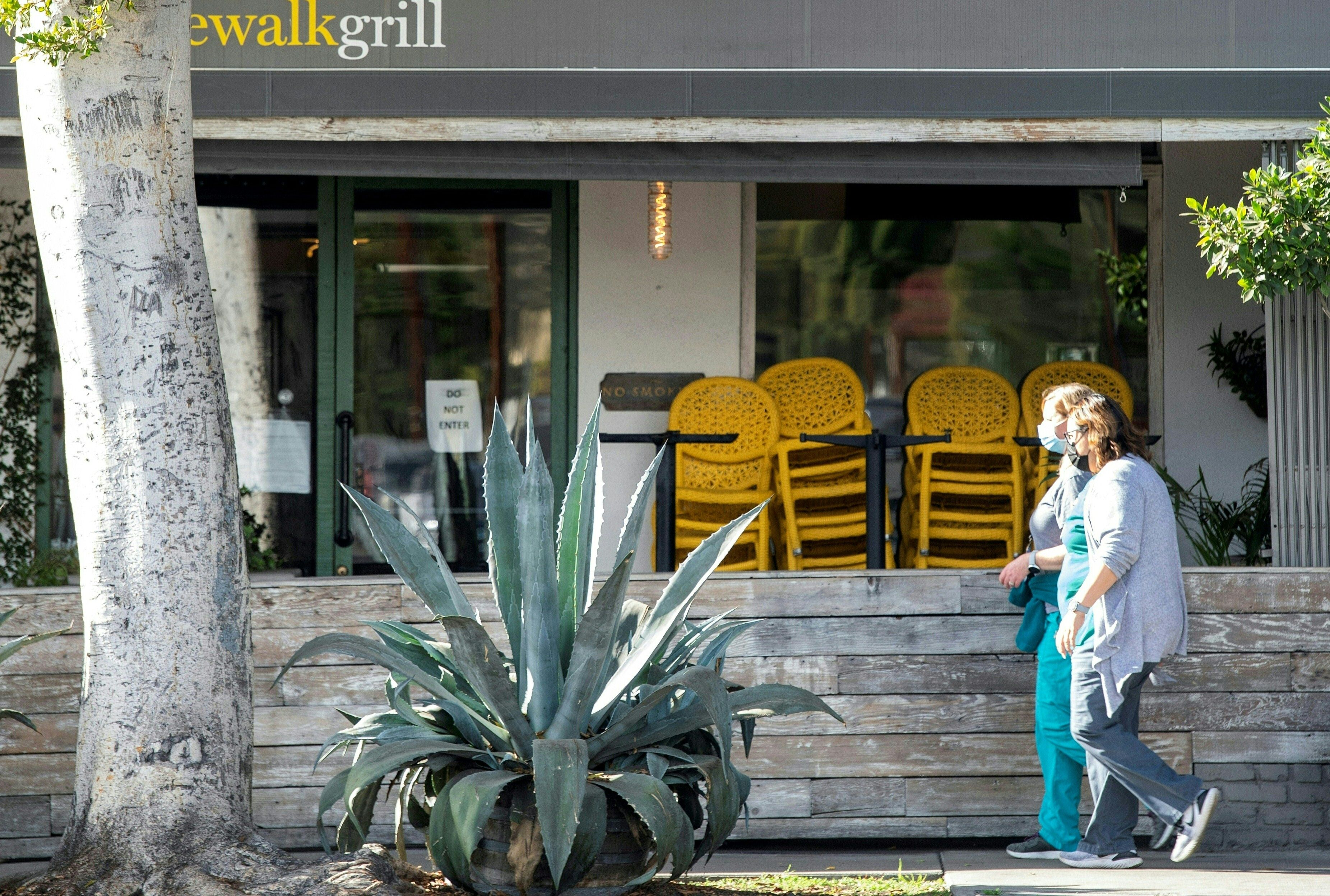 People wearing face masks walk past a closed restaurant in Los Angeles amid Southern California's stay-at-home regulation on Dec. 8, 2020. (VALERIE MACON/AFP via Getty Images)