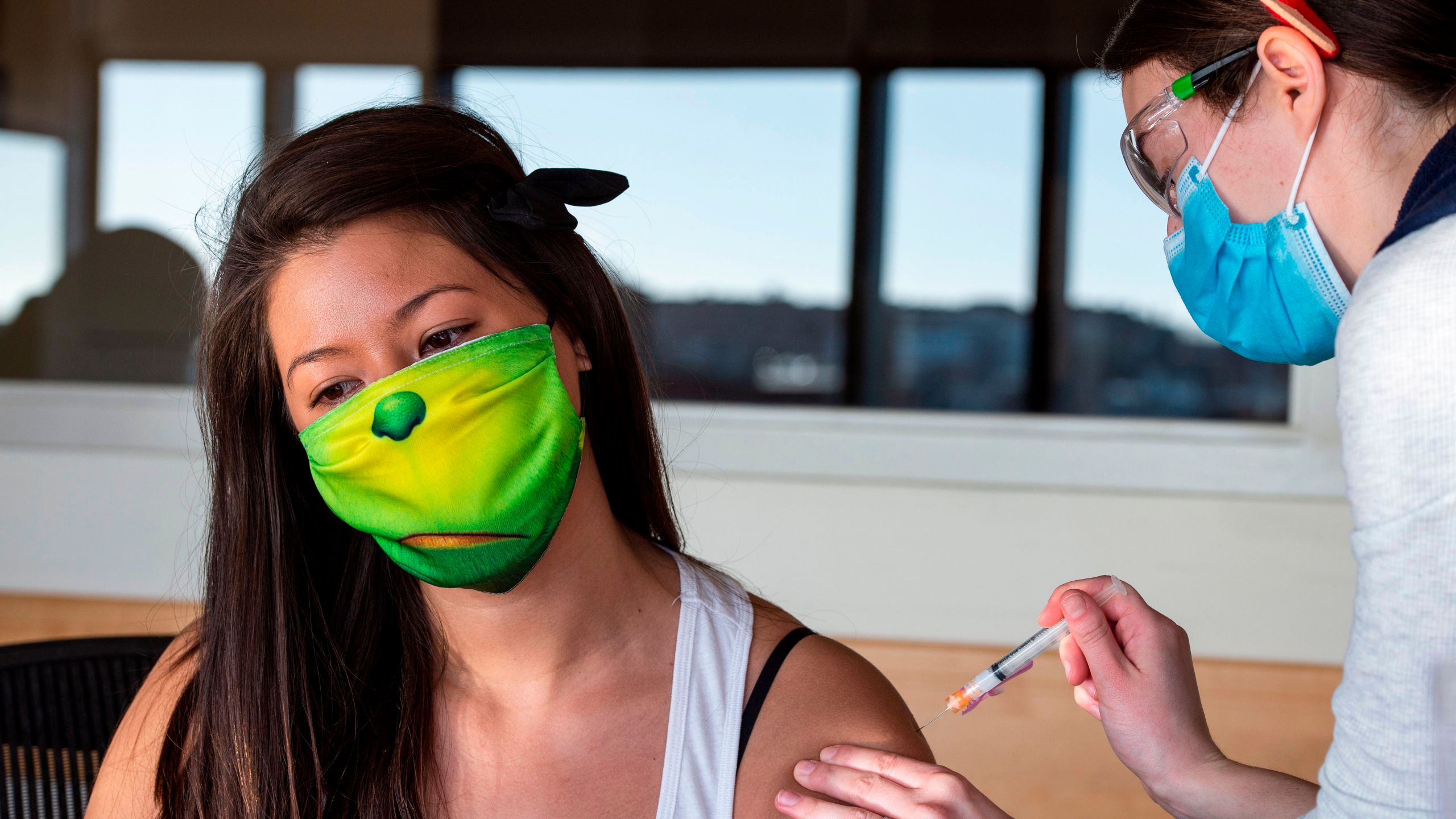 RN Lucia Gleason (R), in her antler headpiece, inoculates PACE worker Jeanne Cooke (L), in a Grinch mask, with the Moderna Covid-19 Vaccine at the East Boston Neighborhood Health Center (EBNHC) in Boston, Massachusetts on December 24, 2020. (Joseph Prezioso/AFP via Getty Images)