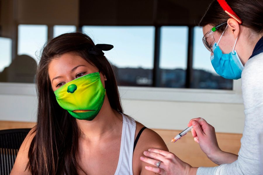 RN Lucia Gleason (R), in her antler headpiece, inoculates PACE worker Jeanne Cooke (L), in a Grinch mask, with the Moderna Covid-19 Vaccine at the East Boston Neighborhood Health Center (EBNHC) in Boston, Massachusetts on December 24, 2020. (Joseph Prezioso/AFP via Getty Images)