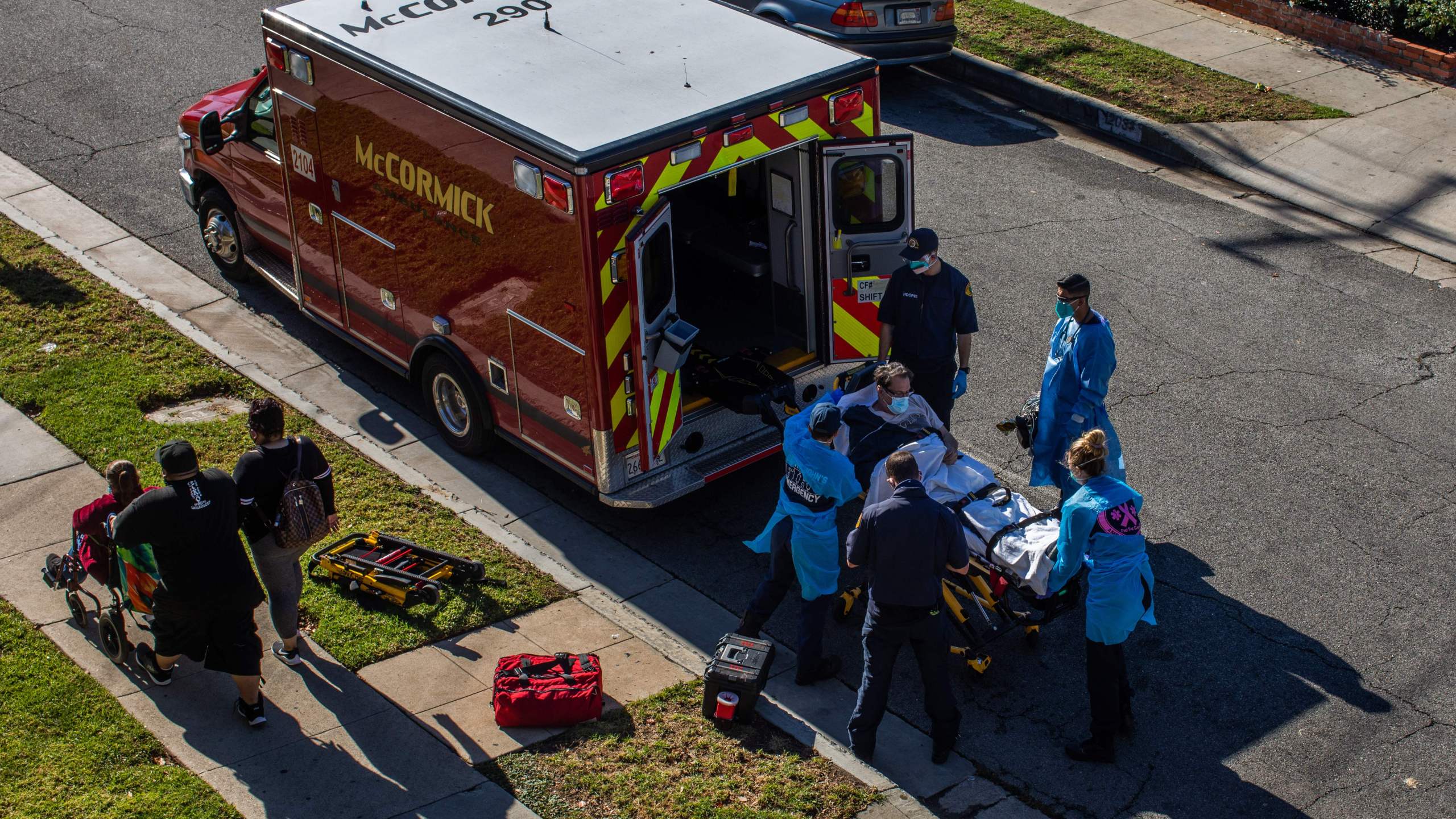 After administering him with oxygen, L.A. County paramedics load a potential COVID-19 patient in the ambulance before transporting him to a hospital in Hawthorne on Dec. 29, 2020 as a family walks by. (APU GOMES/AFP via Getty Images)