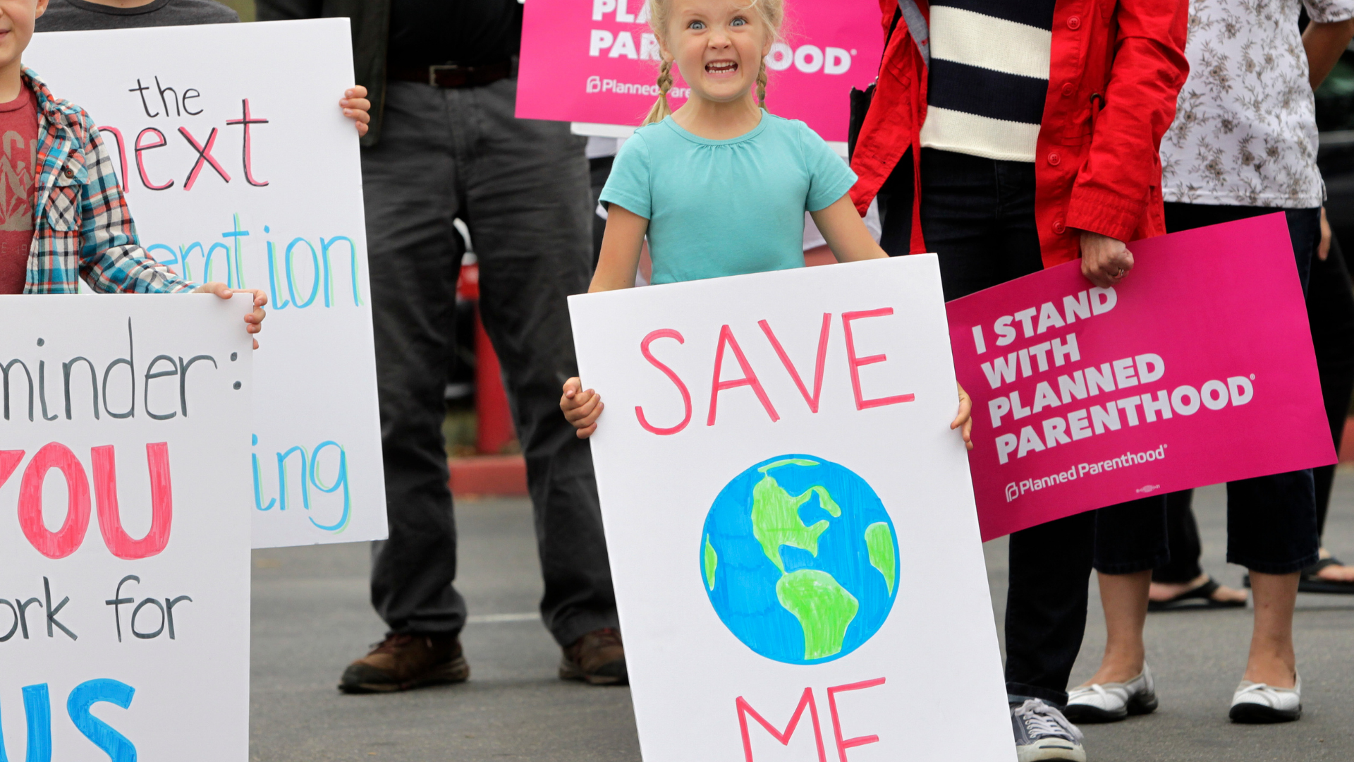 A file photo shows a young girl with a sign that reads "save me" during a demonstration before a town hall meeting with Rep. Darrell Issa at a high school in San Juan Capistrano on June 3, (BILL WECHTER/AFP via Getty Images)