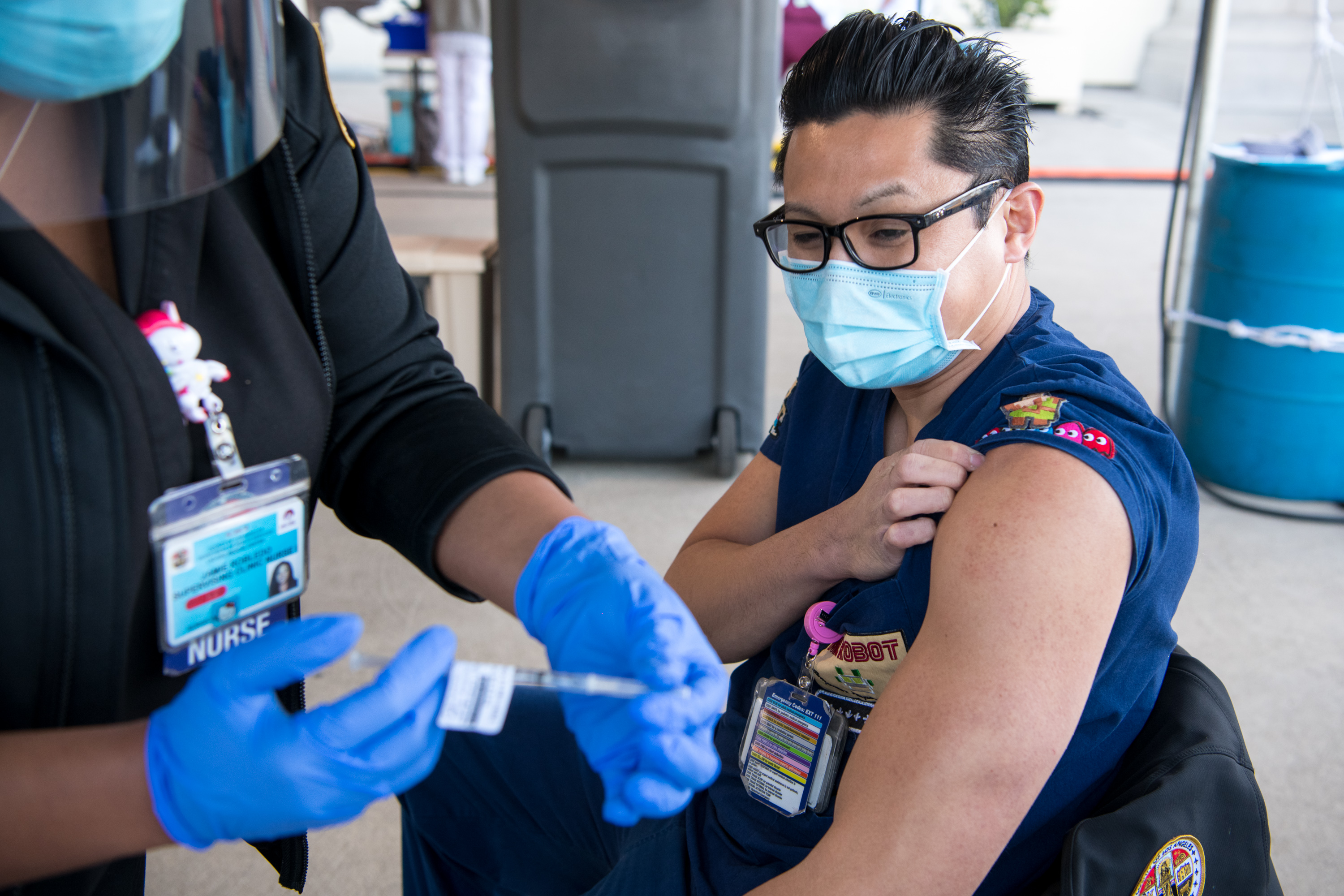 In a handout photo from the Los Angeles County Department of Health Services, Supervising Clinic Nurse Jamie Robledo administers a COVID-19 vaccination to RN Michael Nguyen at LAC+USC Medical Center on Dec. 18, 2020. (Michael Owen Baker)