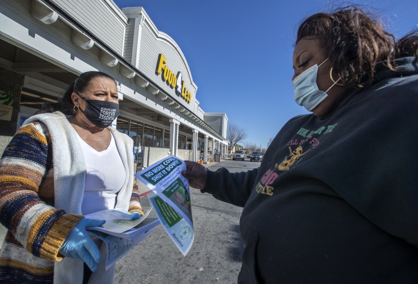 Barbara Hughes, left, a cashier at Food 4 Less in Palmdale, hands a flier to customer Rona Millage of Palmdale on Friday, notifying her about cases of COVID-19 at the store. (Mel Melcon / Los Angeles Times)