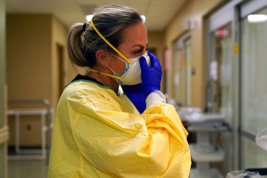 Registered nurse Chrissie Burkhiser puts on personal protective equipment as she prepares to treat a COVID-19 patient in the emergency room at Scotland County Hospital in Memphis, Mo. U.S. hospitals slammed with COVID-19 patients are trying to lure nurses and doctors out of retirement and recruiting nursing students and new graduates who have yet to earn their licenses. (AP Photo/Jeff Roberson, File)