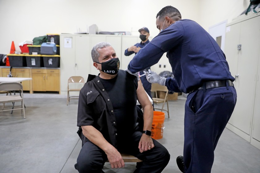 John Novela, a Los Angeles Fire Department fire inspector, receives a COVID-19 vaccination given by Mario Guillen, an LAFD firefighter paramedic in Dec. 2020.(Gary Coronado / Los Angeles Times)