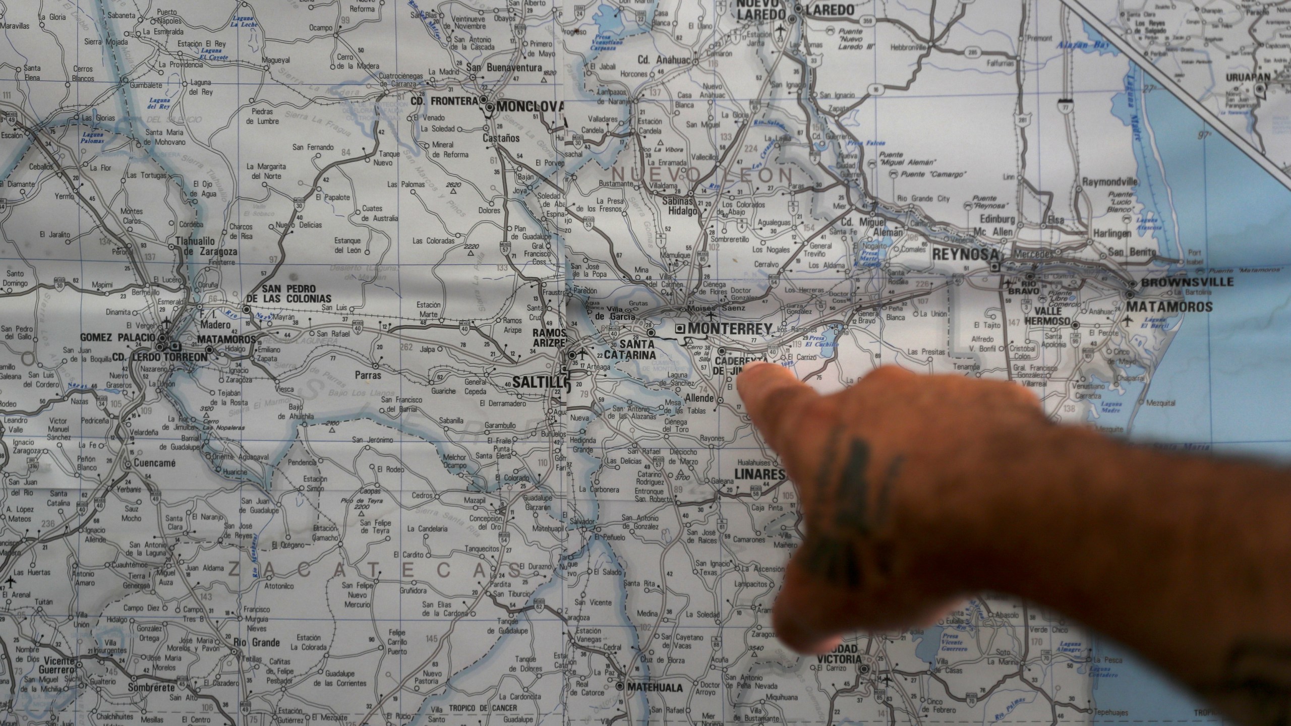 In this Oct. 10, 2019 photo, a Mexican migrant points to a map of U.S.-Mexico border cities, hanging on display at a migrant shelter in Reynosa, Mexico. The Mexican state of Tamaulipas used to be a crossroads. Its dangers are well known. (AP Photo/Fernando Llano)