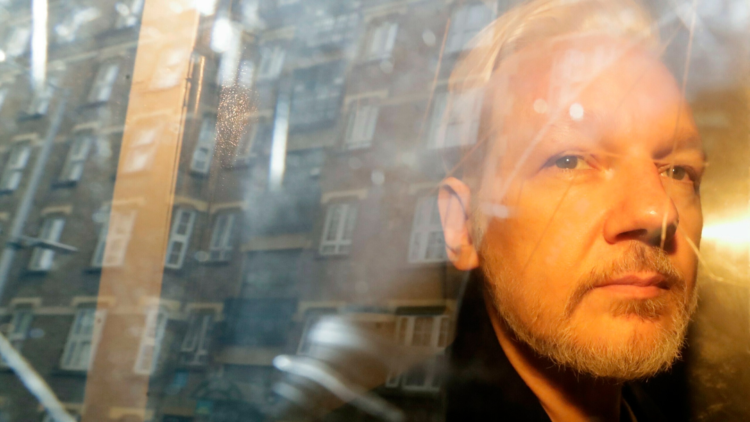 In this Wednesday May 1, 2019 file photo, buildings are reflected in the window as WikiLeaks founder Julian Assange is taken from court, where he appeared on charges of jumping British bail seven years ago, in London. (Matt Dunham/AP Photo)