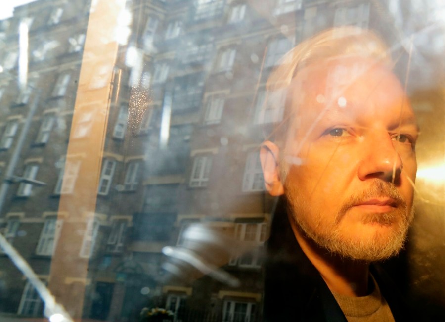 In this Wednesday May 1, 2019 file photo, buildings are reflected in the window as WikiLeaks founder Julian Assange is taken from court, where he appeared on charges of jumping British bail seven years ago, in London. (Matt Dunham/AP Photo)