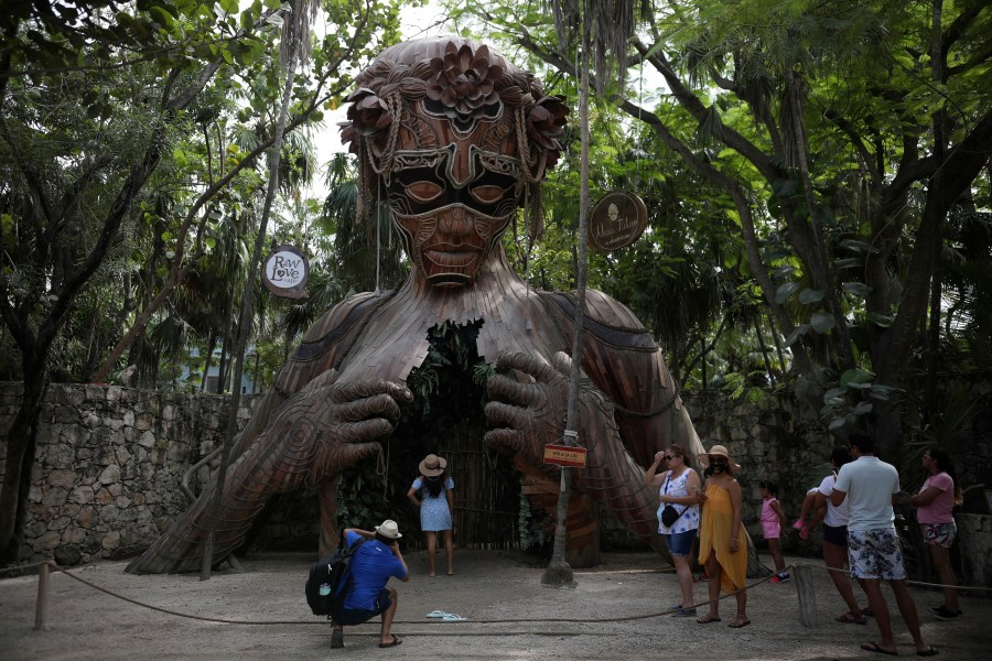 Tourists wait their turn to pose for a photo with a figurative sculpture that serves as an archway by South African artist Daniel Popper titled, "Ven a la Luz" at the Ahau Tulum resort, Quintana Roo, Mexico on Jan. 4, 2021. (Emilio Espejel/Associated Press)