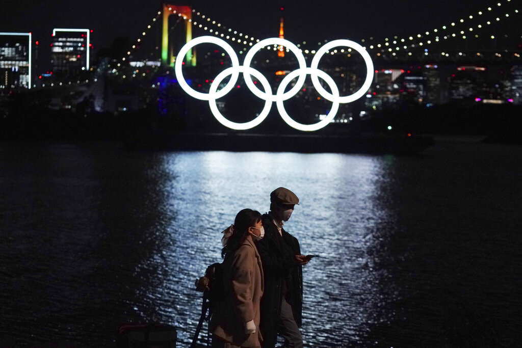 In this Dec. 1, 2020, file photo, a man and a woman walk past near the Olympic rings floating in the water in the Odaiba section in Tokyo. (AP Photo/Eugene Hoshiko, File)