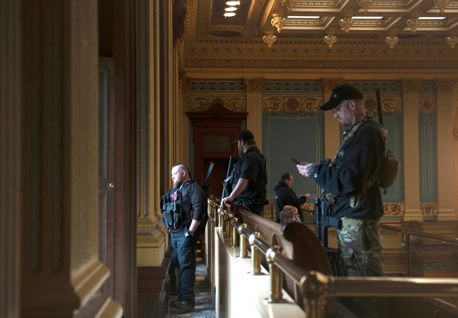 In this April 30, 2020, file photo, armed members of a militia group watch the protest outside while waiting for the Michigan Senate to vote at the Capitol in Lansing, Mich. Michigan has banned the open carry of guns in the state Capitol a week after an armed mob rioted in the U.S. Capitol and following an attempt to storm the statehouse last year. (Nicole Hester/MLive.com/Ann Arbor News via AP File)