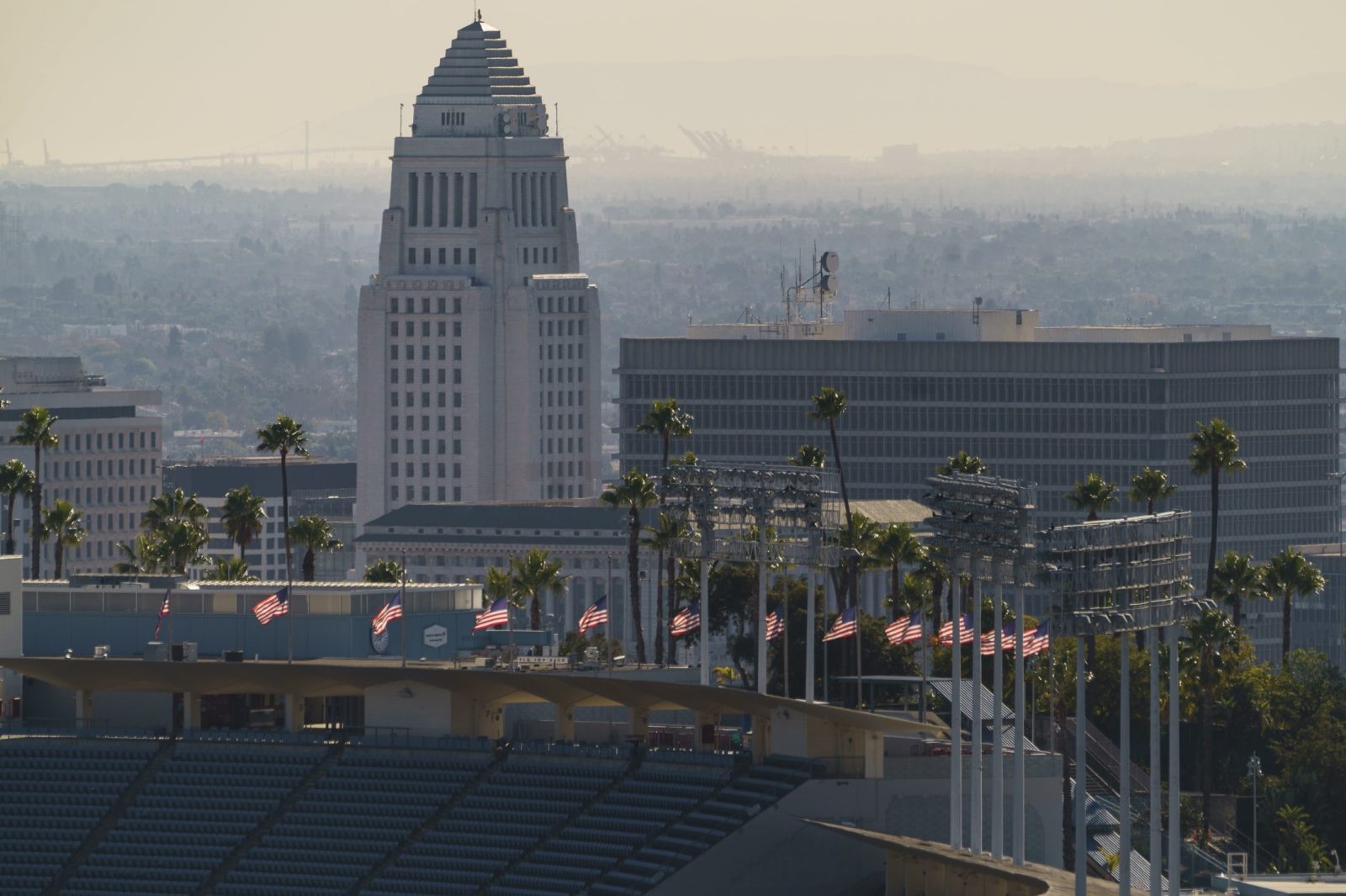 Flags fly half-mast at Dodgers Stadium in honor of the recent passing of the Hall of Fame manager Tommy Lasorda overlooking Los Angeles City Hall Monday, Jan. 11, 2021. Dodger Stadium, the home stadium of Major League Baseball's Los Angeles Dodgers holds 56,000 spectators. The The coronavirus death toll in California reached 30,000 on Monday, another staggering milestone as the nation's most populous state endures the worst surge of the nearly yearlong pandemic. (AP Photo/Damian Dovarganes)