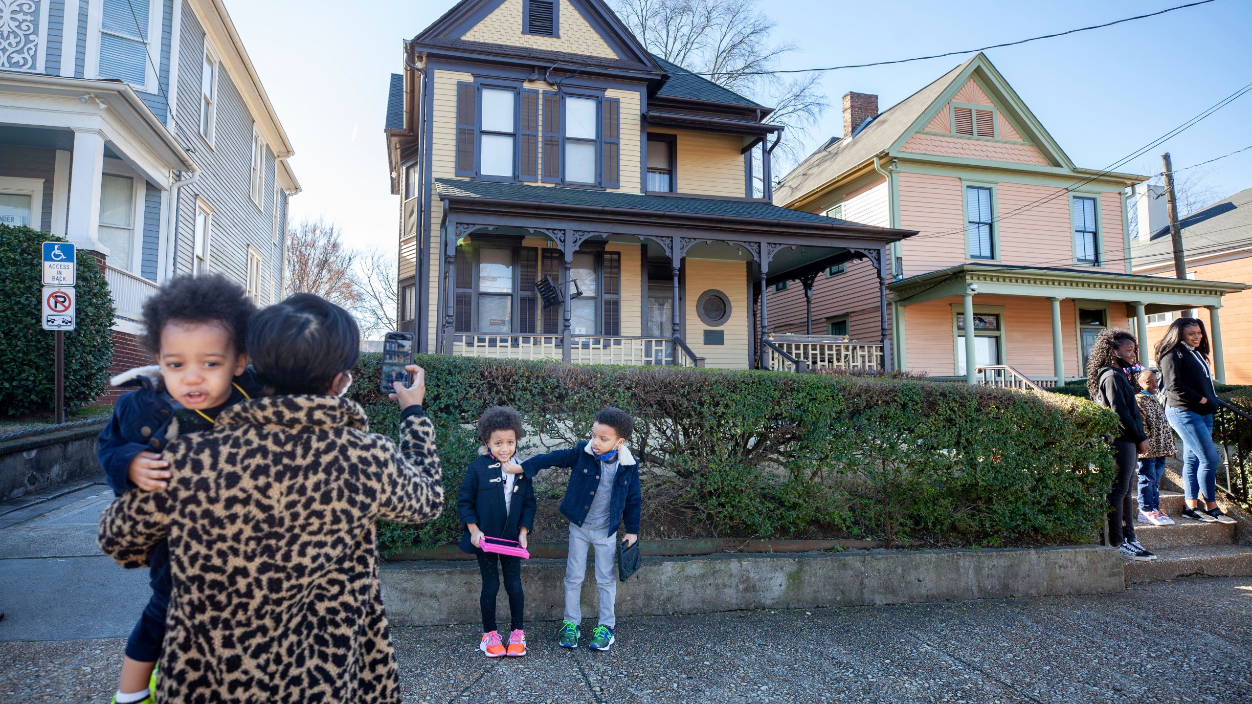 Alexis Upshaw, left, holding 2-year-old Ari Upshaw, takes a photo as Ty Upshaw, 7, right, adjusts the mask of his sister, Mila Upshaw, 5, in front of the birthplace of Dr. Martin Luther King, Jr. on Monday, Jan. 18, 2021, the Martin Luther King Jr. holiday, in Atlanta. (AP Photo/Branden Camp)