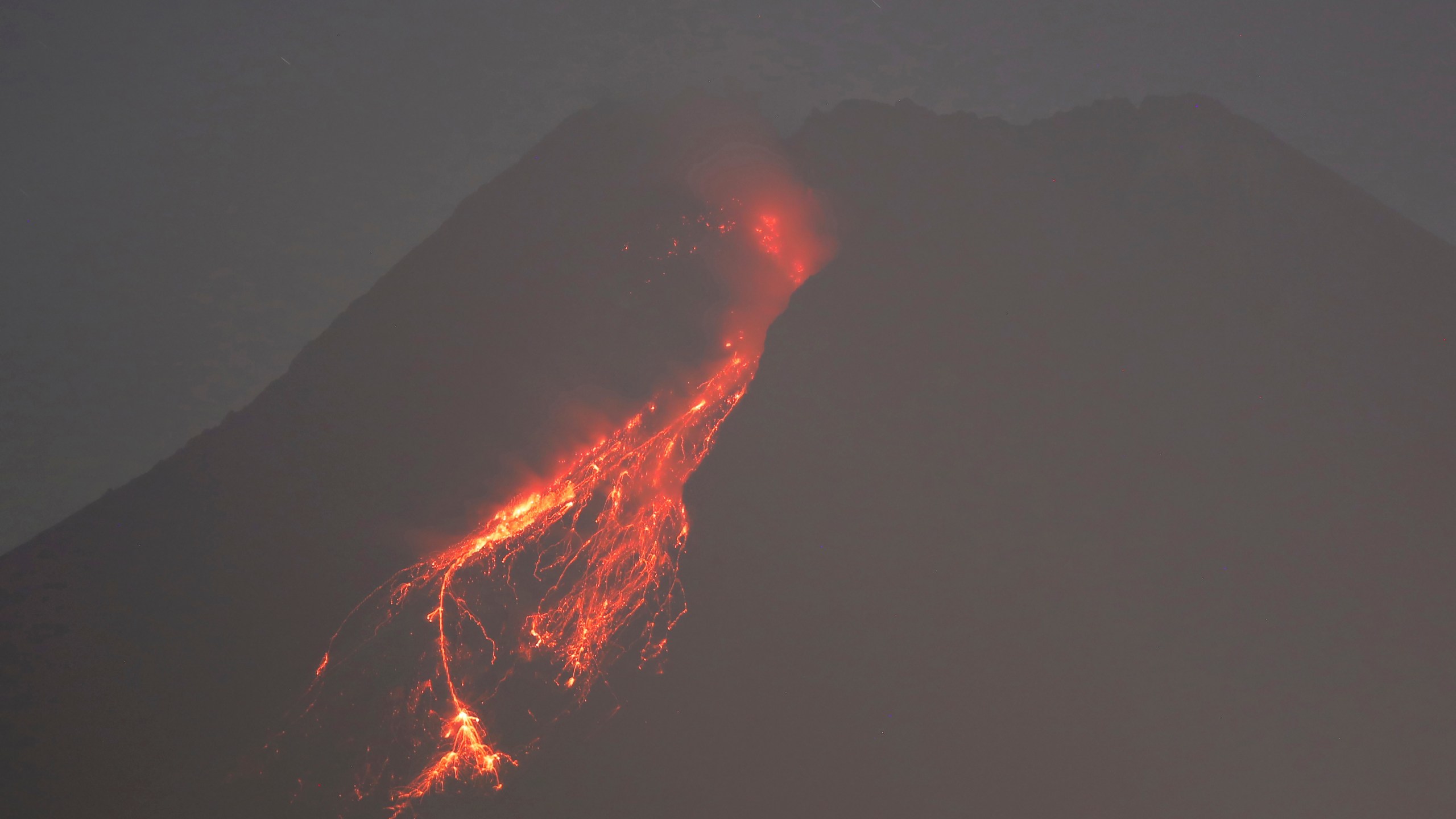 In this time-lapsed photo, hot lava runs down the side of Mount Merapi as its activity continues since local geological authority raised the alert level to the second-highest level in November, in Kaliurang, Indonesia, early Sunday, Jan. 24, 2021. Merapi is one of the most volatile among the country's more than 120 volcanoes. (AP Photo/Trisnadi)