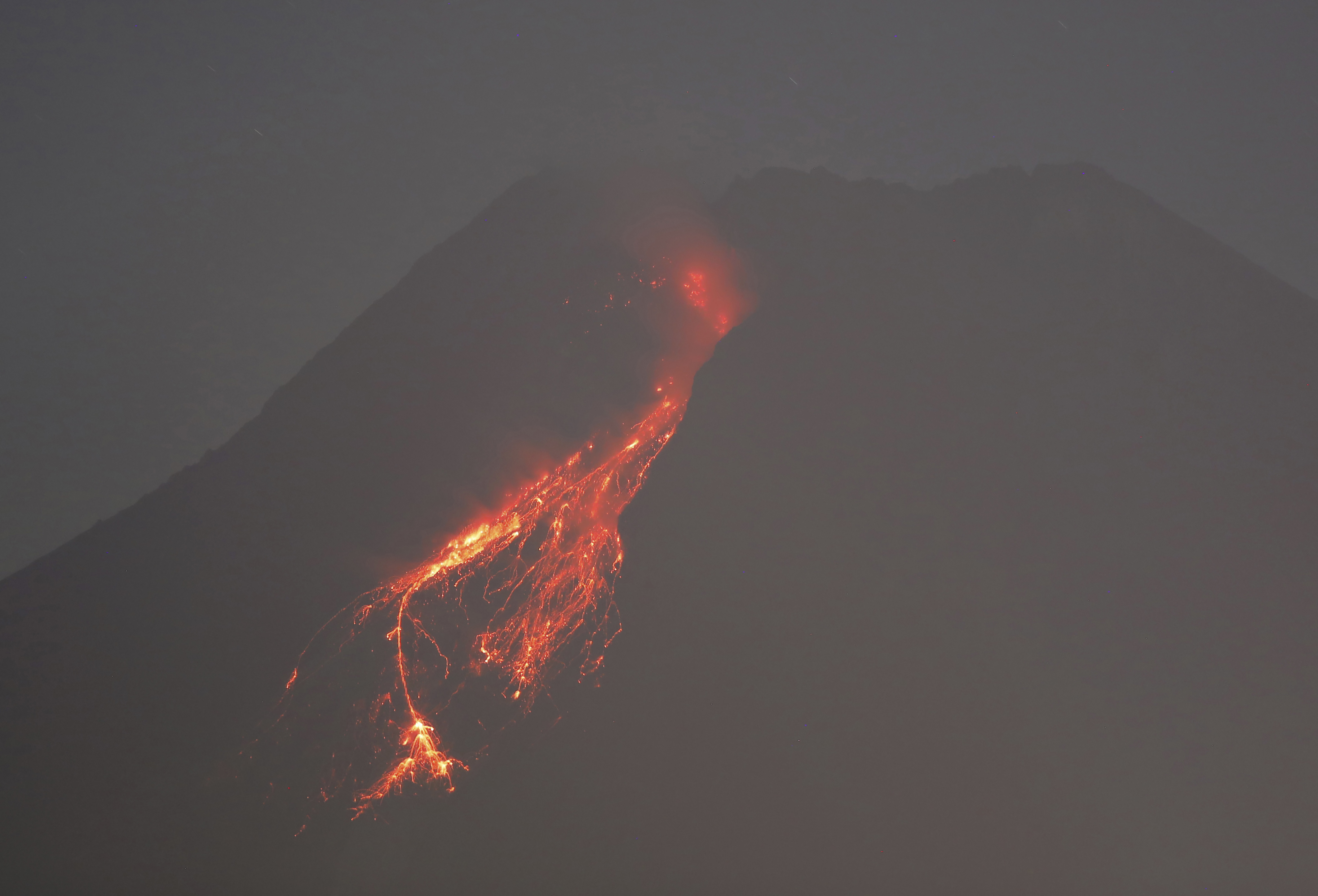 In this time-lapsed photo, hot lava runs down the side of Mount Merapi as its activity continues since local geological authority raised the alert level to the second-highest level in November, in Kaliurang, Indonesia, early Sunday, Jan. 24, 2021. Merapi is one of the most volatile among the country's more than 120 volcanoes. (AP Photo/Trisnadi)