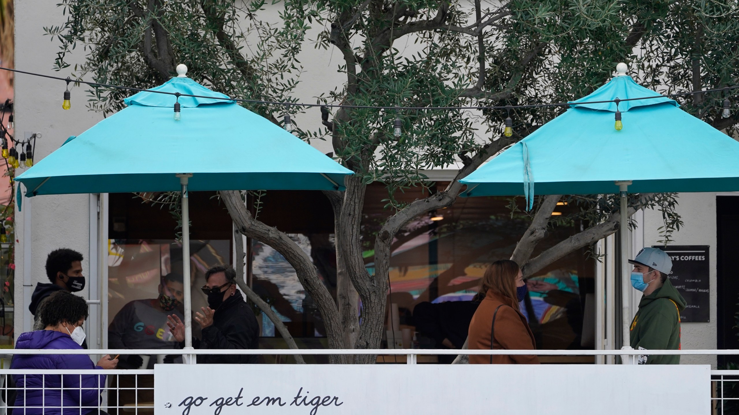 People wear masks as they wait outdoors for takeaway coffee and eats at the "go get em tiger" coffee bar on Hollywood Blvd., in Los Angeles Monday, Jan. 25, 2021. (AP Photo/Damian Dovarganes)