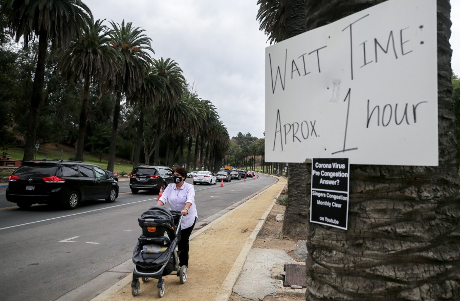 A woman pushes a stroller past vehicles lined up to enter a COVID-19 testing site at Dodger Stadium on Dec. 7, 2020 in Los Angeles.(Photo by Mario Tama/Getty Images)