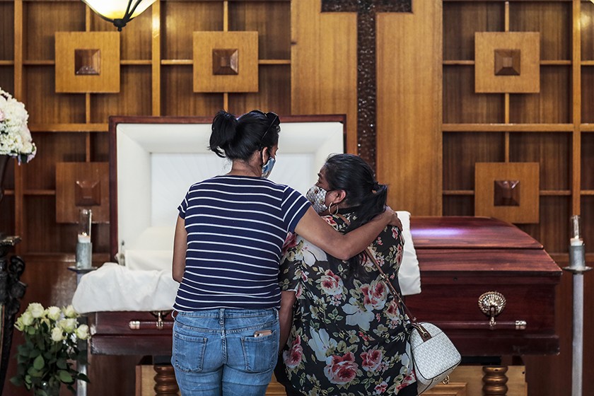 Iris Martinez, right, stands with her friend Grace Salgado before the casket of Martinez’s father, Rafael Martinez, who died of COVID-19. (Robert Gauthier / Los Angeles Times)