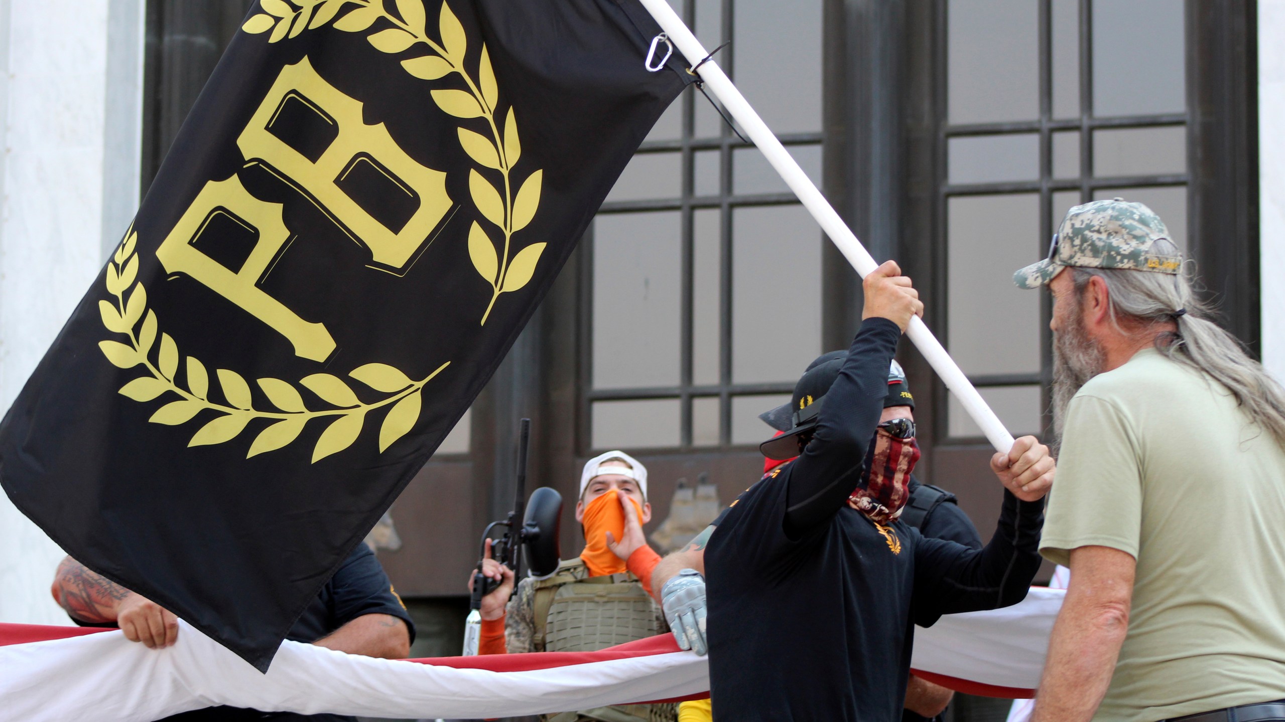 In this Sept. 7, 2020, file photo, a protester carries a Proud Boys banner, a right-wing group, while other members start to unfurl a large U.S. flag in front of the Oregon State Capitol in Salem. (Andrew Selsky/Associated Press)