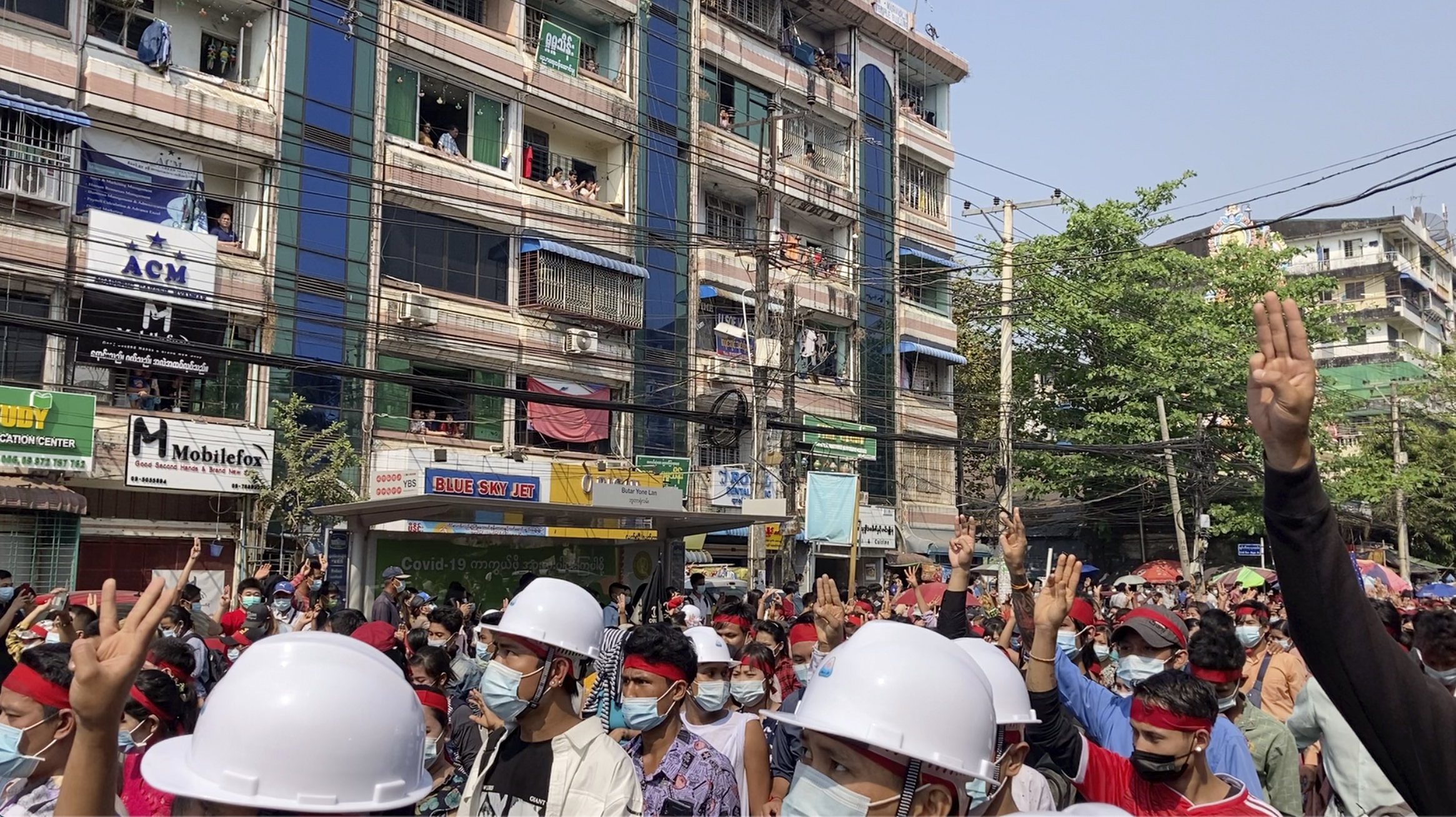 In this image from video, residents watch from their balconies as protesters flashing three-fingered salutes march past Saturday, Feb. 6, 2021, in Yangon, Myanmar. (AP Photo)