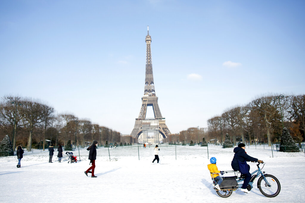 People walk and ride a bicycle on a snow covered alley near the Eiffel Tower, in Paris, Wednesday, Feb. 10, 2021. (AP Photo/Thibault Camus)