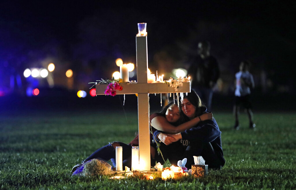 In this Feb. 15, 2018 file photo, people comfort each other as they sit and mourn at one of seventeen crosses, after a candlelight vigil for the victims of the shooting at Marjory Stoneman Douglas High School, in Parkland, Fla. (AP Photo/Gerald Herbert, File)