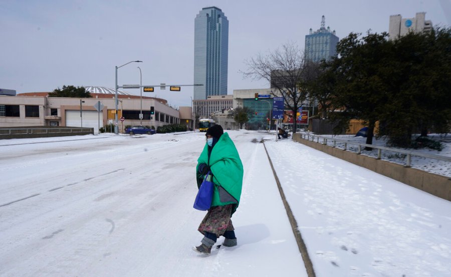 In this Feb. 16, 2021, file photo, a woman wrapped in a blanket crosses the street near downtown Dallas. (AP Photo/LM Otero, File)