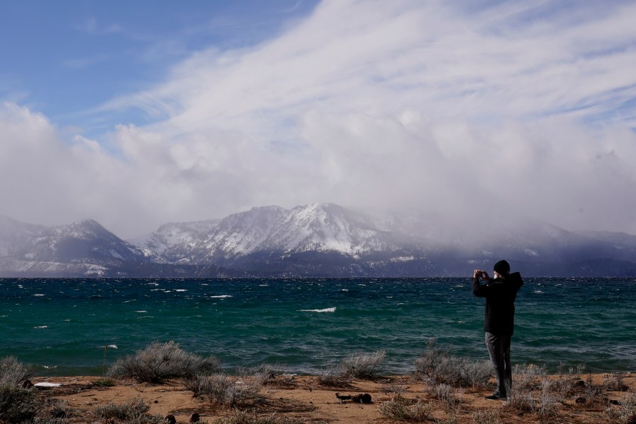 In this Friday, Feb. 19, 2021 file photo, a person takes in the view of Lake Tahoe along the shore of the Edgewood Tahoe Resort, in Stateline, Nev. Researchers at Lake Tahoe are gaining confidence in a new weapon in their arsenal to combat the spread of invasive weeds that rob the alpine lake of its clarity, tiny bubbles. Conservationists are partnering with local property owners to expand the use of the so-called "bubble curtains" to halt the spread of non-native plants in the waters straddling the California-Nevada line, the Tahoe Daily Tribune reports. (AP Photo/Rich Pedroncelli, File)