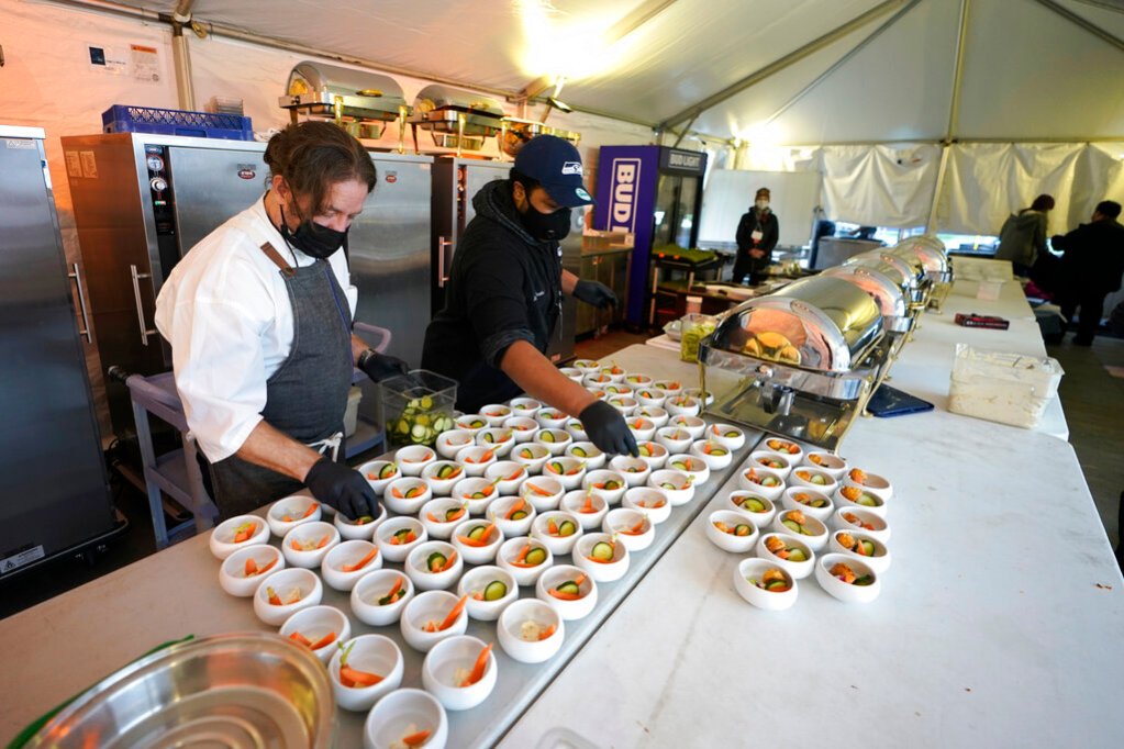 Jason Wilson, left, a chef at The Lakehouse, a restaurant located in Bellevue, Wash., and sous chef Demetrius Parker, right, prepare dishes for the first course of a meal for diners in an outdoor tent set up on the turf at Lumen Field, Thursday, Feb. 18, 2021, in Seattle. (AP Photo/Ted S. Warren)