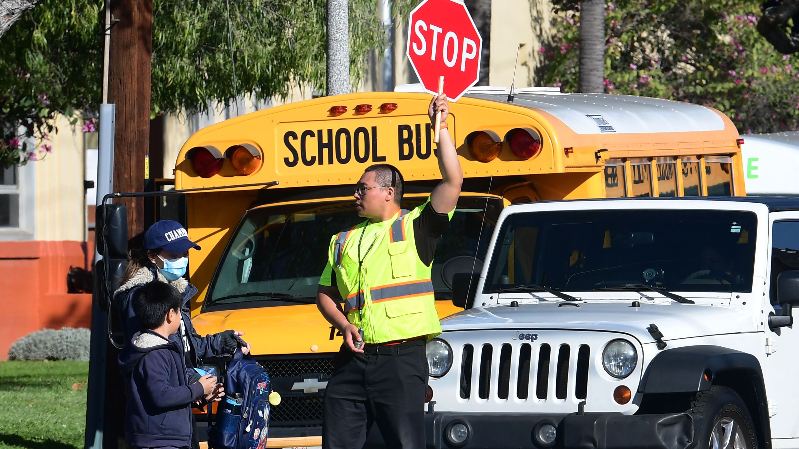 A woman wears a facemask picking up a child as an Alhambra Unified School District crossing guard stops traffic outside Ramona Elementary School on February 4, 2020 in Alhambra, California. (Photo by Frederic J. BROWN / AFP)