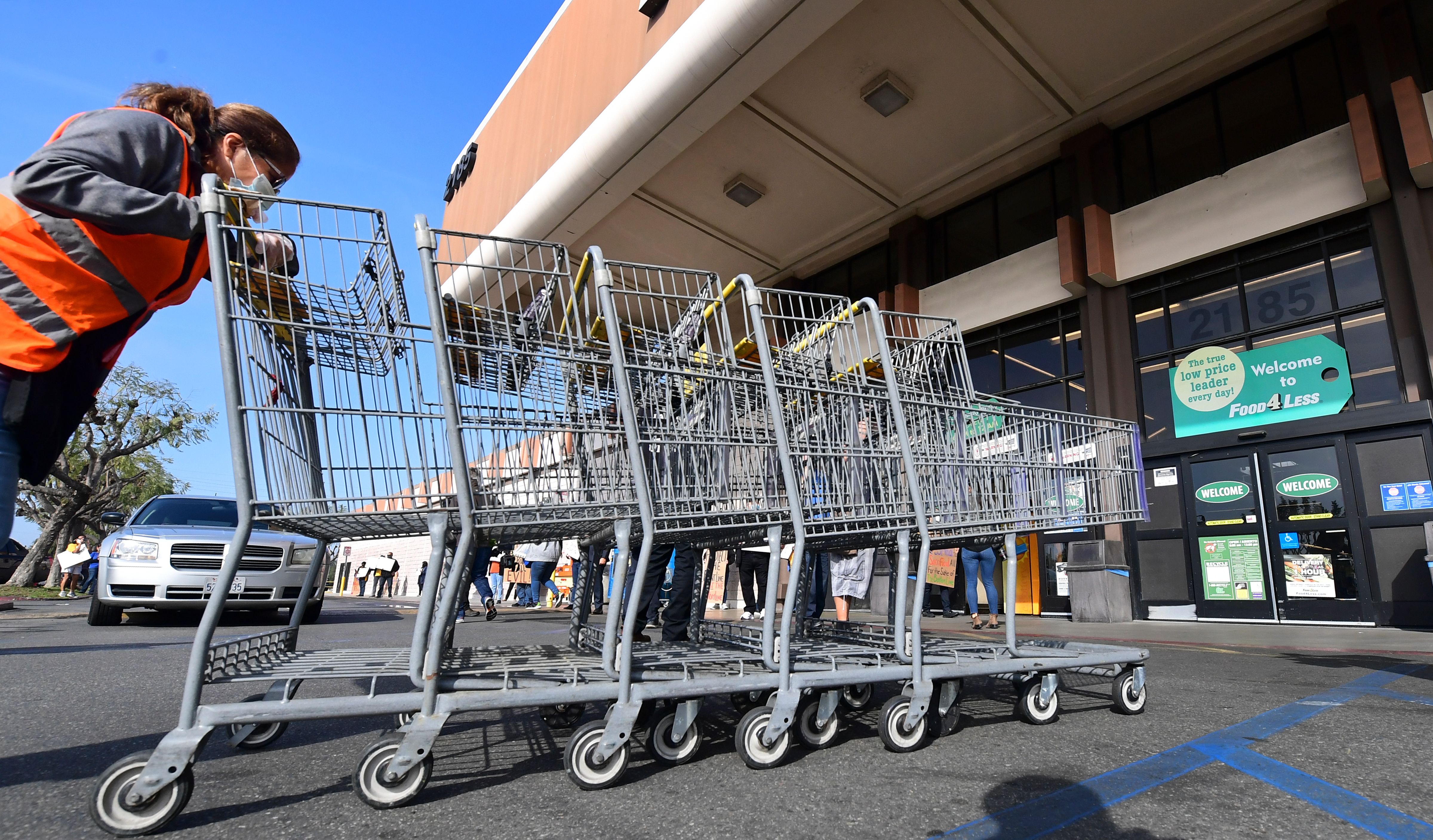 A Food 4 Less employee pushes carts past supermarket workers gathered to protest in front of the supermarket in Long Beach on Feb. 3, 2021, after a decision by owner Kroger to close two supermarkets rather than pay workers an additional $4 in "hazard pay." (Frederic J. Brown / AFP / Getty Images)