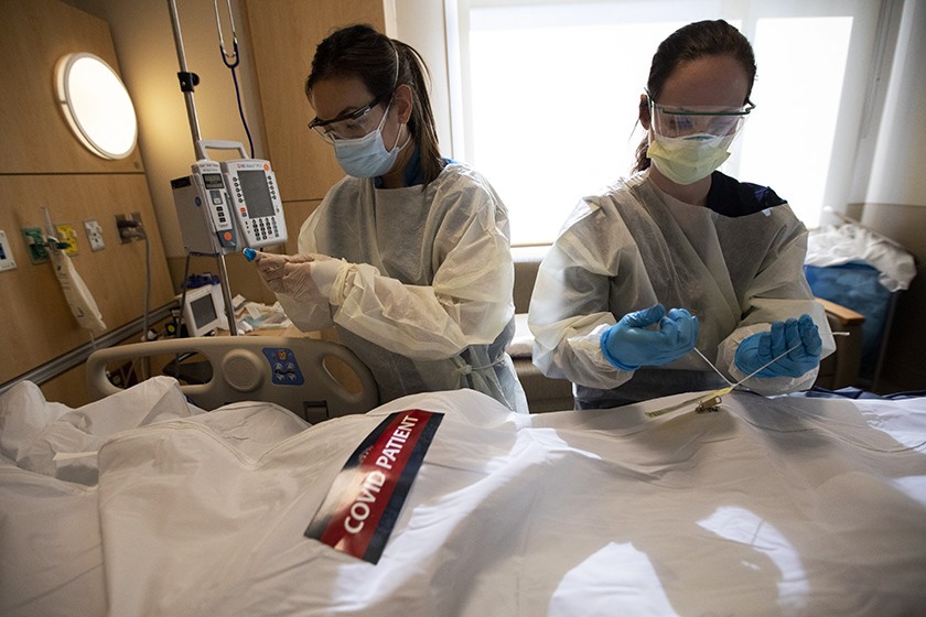 Registered nurses April McFarland, left, and Tiffany Robbins place the body of a COVID-19 victim inside a white bag and zip it closed at Providence Holy Cross Medical Center in Mission Hills.(Francine Orr / Los Angeles Times)