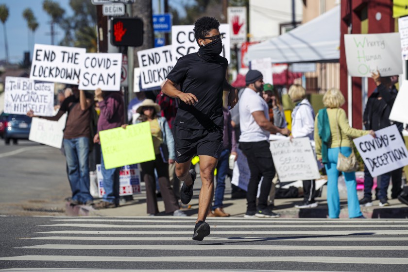 Thomas Miller jogs by demonstrators at a rally, organized by Shop Mask Free Los Angeles, to protest the COVID-19 vaccine, masks and lockdowns on Sunset Boulevard near Dodger Stadium on Jan. 30, 2021. (Irfan Khan / Los Angeles Times)