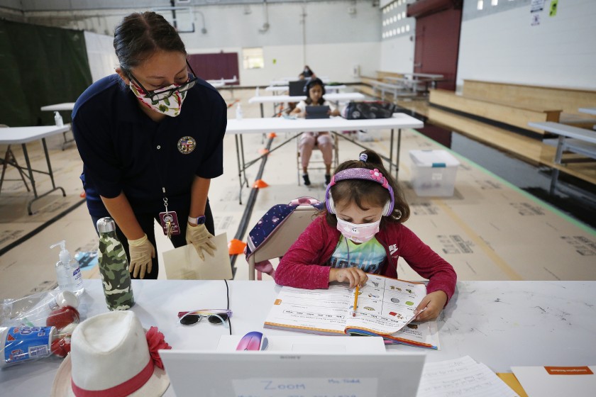 First-grader April Alvarez logs into online classes in September 2020 from the Delano Recreation Center in Van Nuys, with help from Astrid Gramajo. (Al Seib / Los Angeles Times)