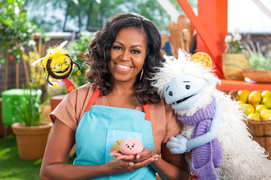 This image released by Netflix shows former first lady Michelle Obama with Busy, a bee puppet, left, Mochi, a pink round puppet, and Waffles, a furry puppet with waffle ears on the set of the children's series "Waffles + Mochi." Obama is launching the new Netflix children’s food show on March 16. (Adam Rose/Netflix via AP)