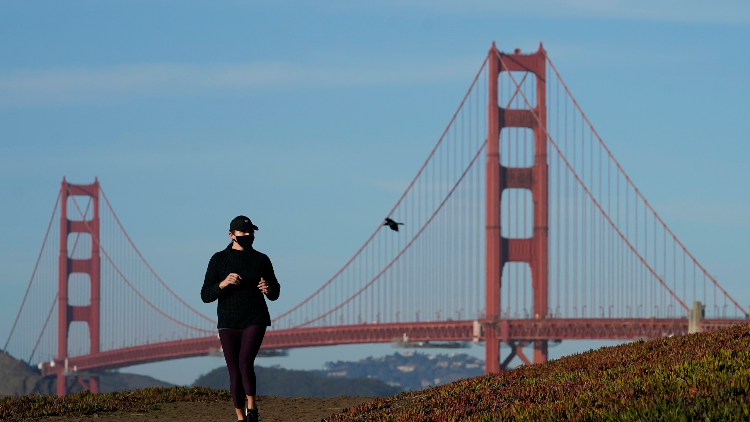 A person wearing a mask runs on a path in front of the Golden Gate Bridge in San Francisco during the coronavirus pandemic on Nov. 30, 2020. (Jeff Chiu / Associated Press)