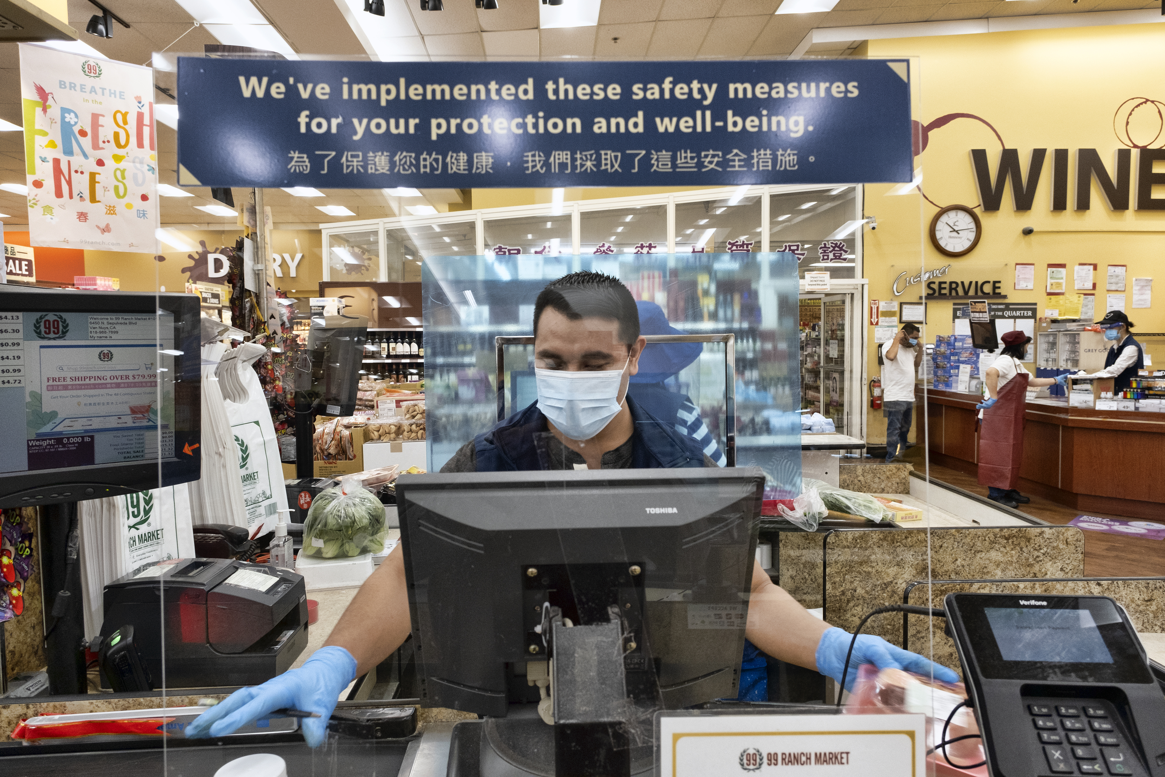 A grocery worker wears a protective mask and gloves as he helps to check out a customer from behind a plexiglass barrier at a market Van Nuys on May 5,2020. (Richard Vogel / Associated Press)