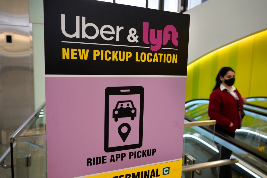 In this Feb. 9, 2021 photo, a passer-by walks past a sign offering directions to an Uber and Lyft ride pickup location at Logan International Airport in Boston. (Steven Senne/Associated Press)