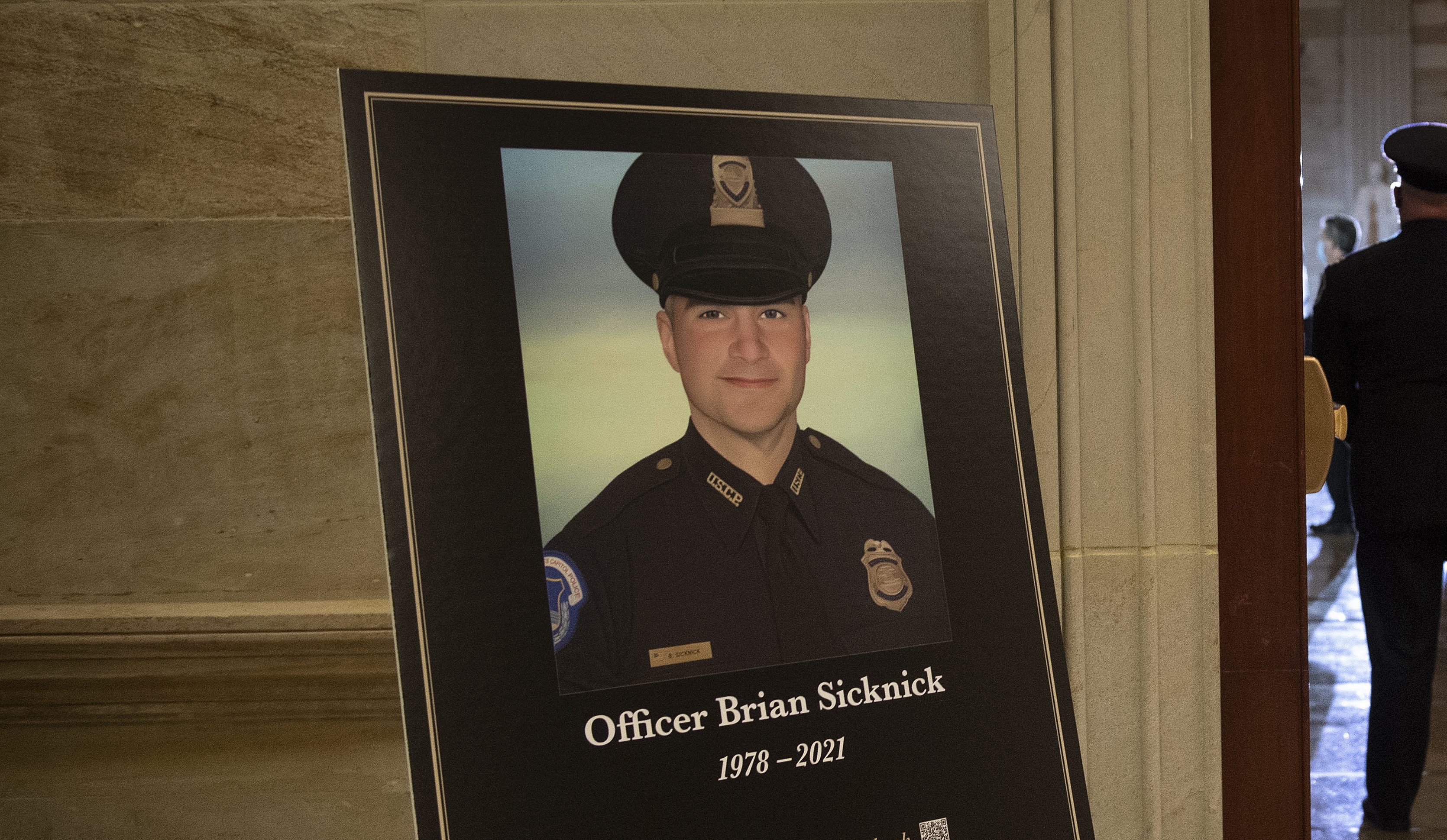 In this Feb. 2, 2021, file photo a placard is displayed with an image of the late U.S. Capitol Police officer Brian Sicknick on it as people wait for an urn with his cremated remains to be carried into the U.S. Capitol to lie in honor in the Capitol Rotunda in Washington. (Brendan Smialowski/Pool via AP, File)