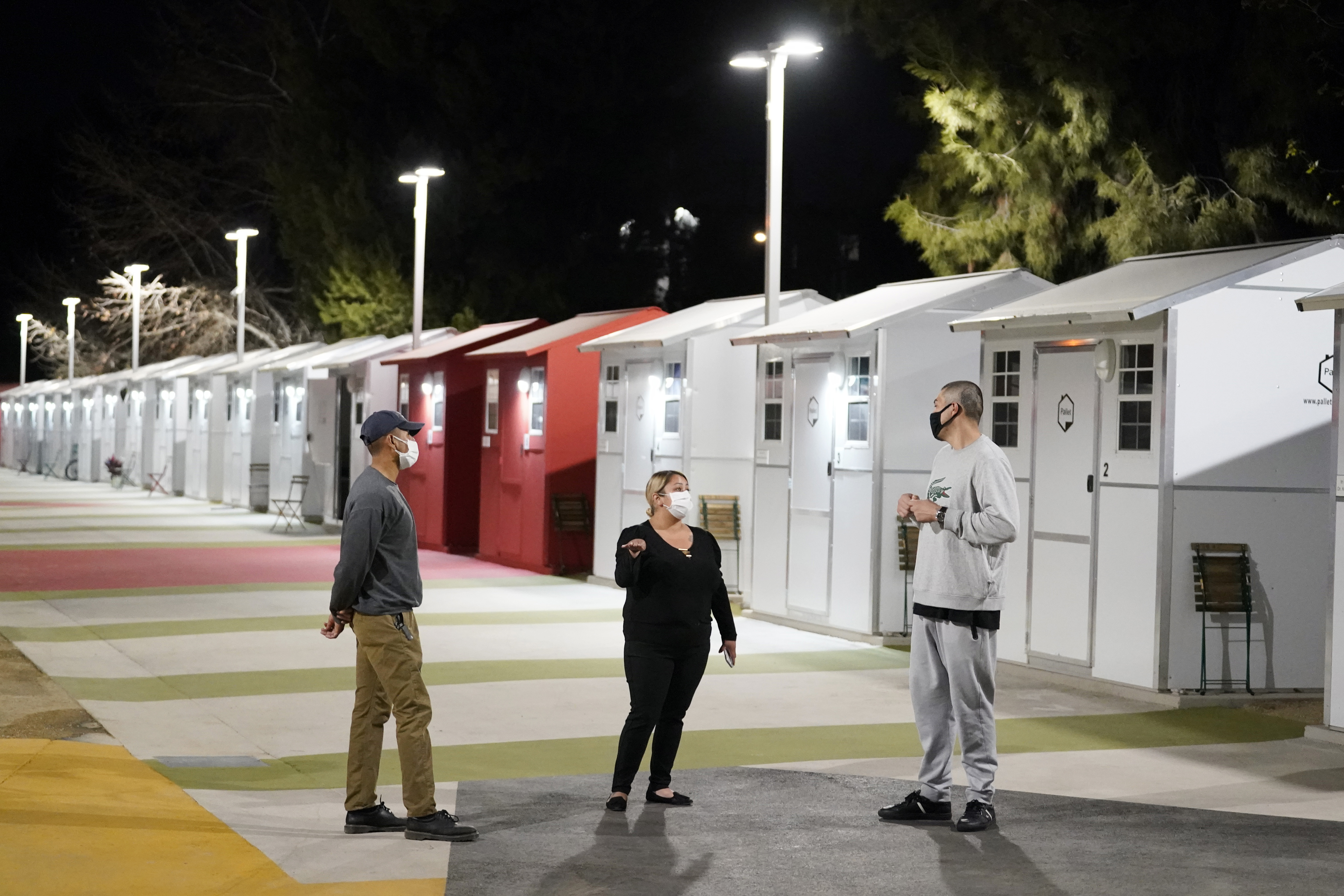 Workers talk to a resident, at right, in front a row of tiny homes for the homeless on Feb. 25, 2021, in North Hollywood. (AP Photo/Marcio Jose Sanchez)