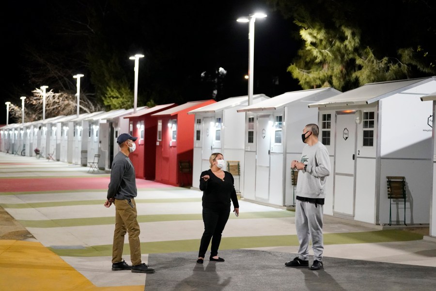 Workers talk to a resident, at right, in front a row of tiny homes for the homeless on Feb. 25, 2021, in North Hollywood. (AP Photo/Marcio Jose Sanchez)